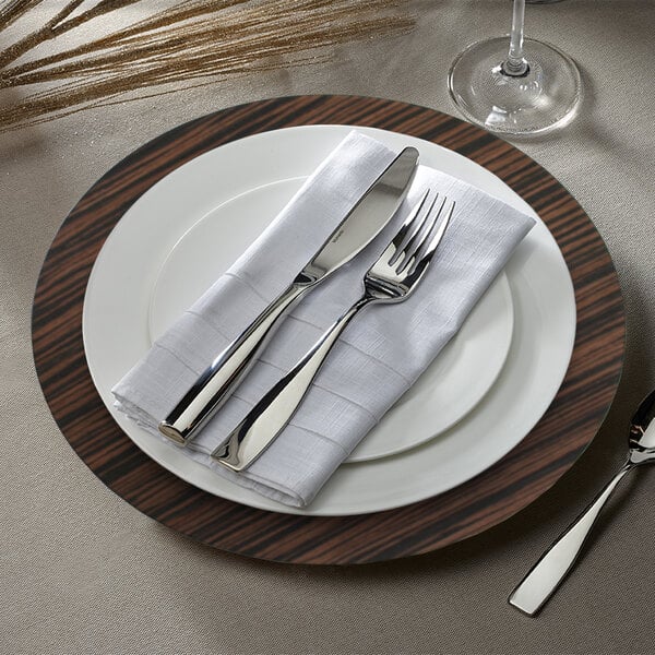 A brown faux wood charger plate with a white napkin and silverware on it.