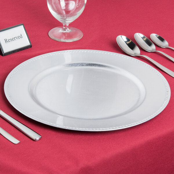 A Charge It by Jay silver beaded plastic charger plate with silverware on a table.
