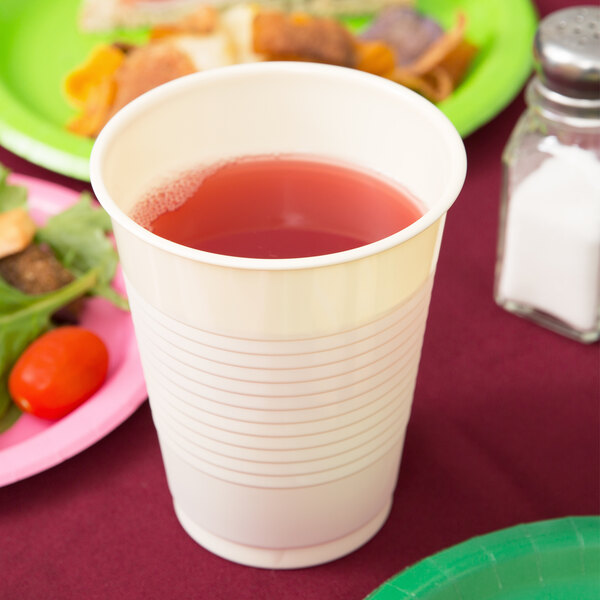 A Creative Converting ivory plastic cup filled with red liquid on a table.