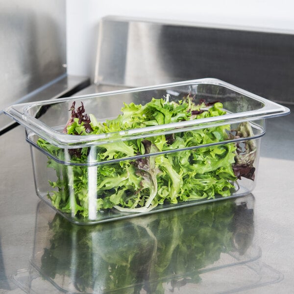 A clear plastic Cambro food pan filled with lettuce on a kitchen counter.