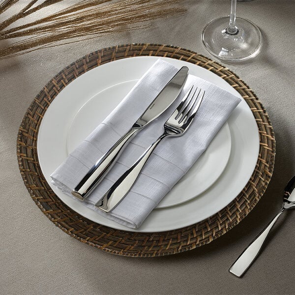 A brick brown rattan charger plate with a white napkin and silverware on it.