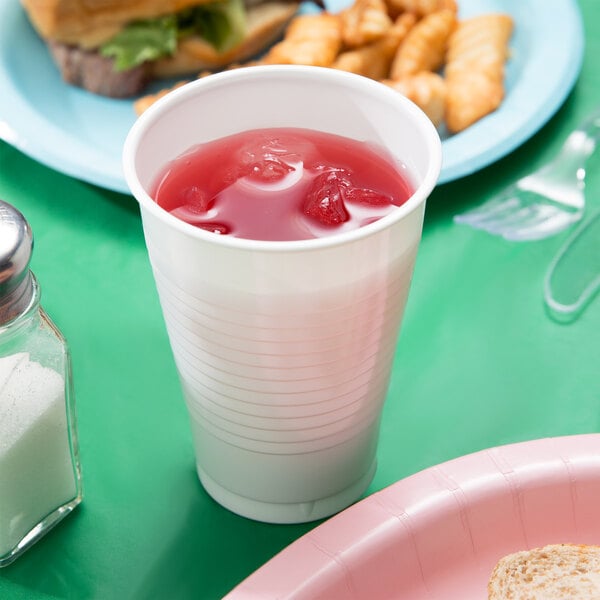 A white plastic cup filled with red liquid next to a plate of food.