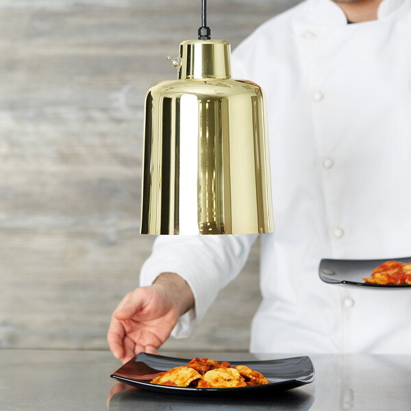 A chef holding plates of food under a brass Hanson Heat Lamp.