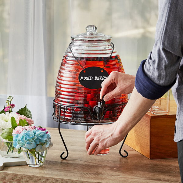 A person pouring red liquid into an Acopa glass beverage dispenser.