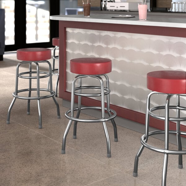 Three Lancaster Table & Seating maroon vinyl double ring swivel bar stools at a counter in a cocktail bar.