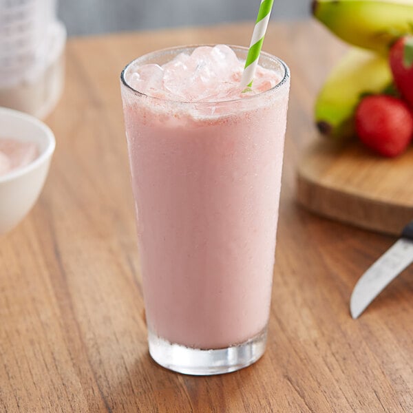 A glass of pink Big Train Strawberry Banana Frappe with a straw on a table.