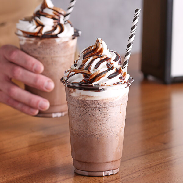 A hand holding a plastic cup of Big Train frozen hot chocolate with whipped cream.