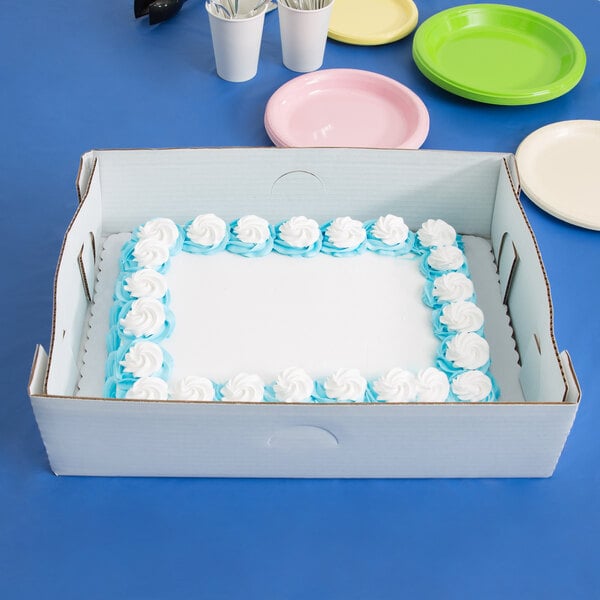 A white frosted cake in a Baker's Mark white corrugated tray in a box.