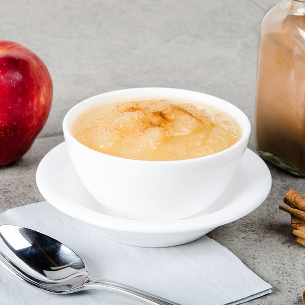 A bowl of Musselman's natural unsweetened applesauce with a spoon on a table.