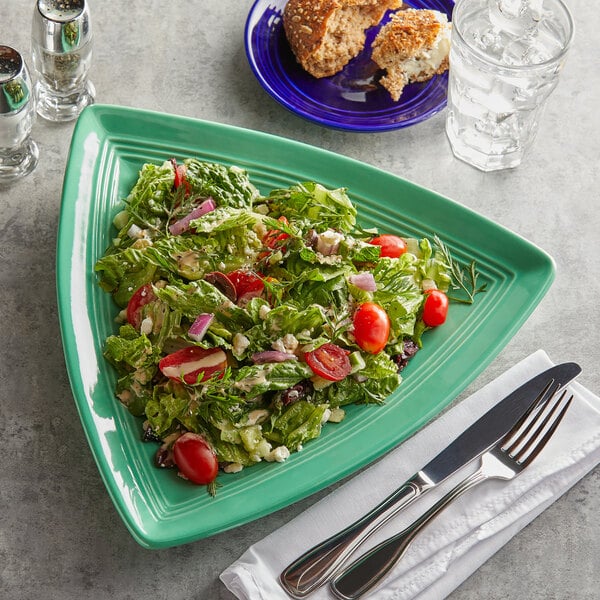 A Tuxton Concentrix cilantro green triangle plate with salad, a fork, and a knife on it.