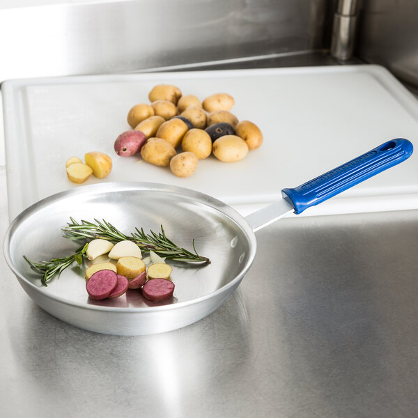 An Vollrath Wear-Ever aluminum fry pan with vegetables cooking in it on a counter.