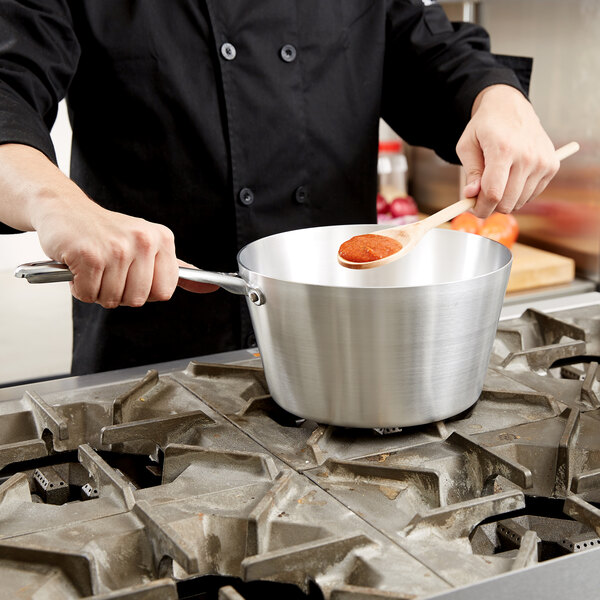 A person cooking red sauce in a Vollrath Wear-Ever sauce pan on a stove with a wooden spoon.
