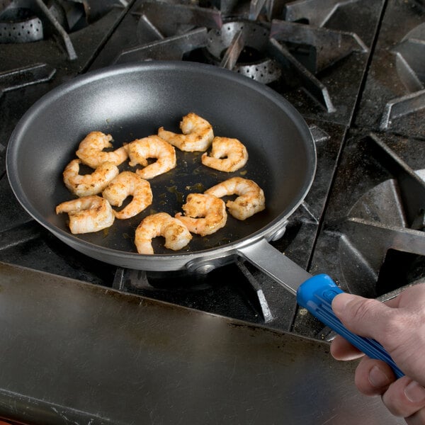 A hand cooking shrimp in a Vollrath Wear-Ever blue handled fry pan.