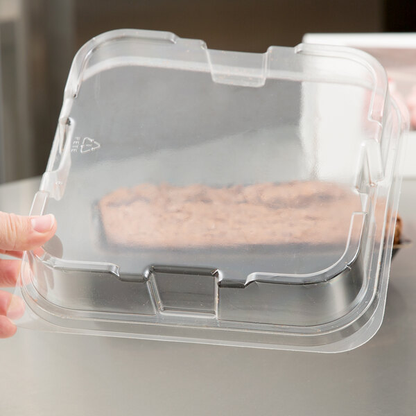 A hand holding a clear plastic container with a cake inside.