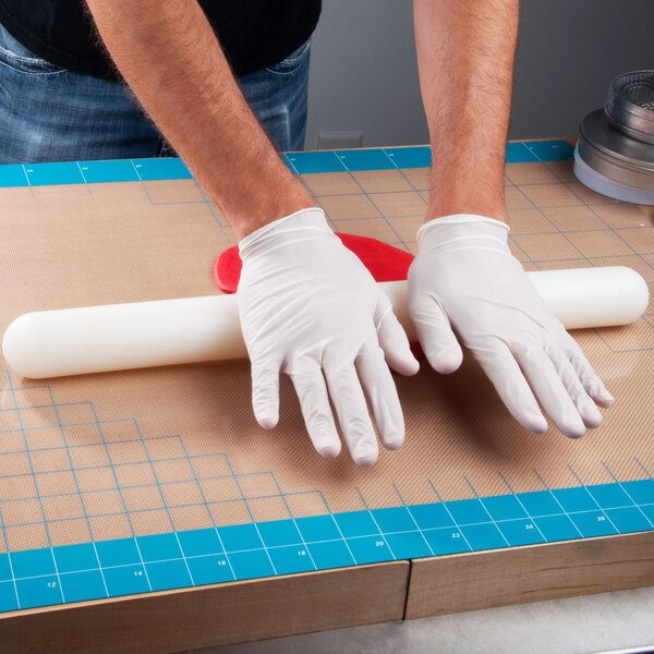 A person wearing white gloves rolls out dough on an Ateco silicone baking mat.
