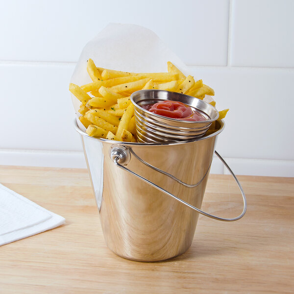A stainless steel mini pail filled with french fries and a bowl of ketchup on a table.