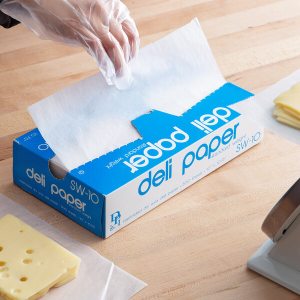 A person's hand in a plastic glove using Durable Packaging Deli Wrap to cut cheese.