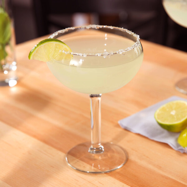 A Libbey Fiesta Grande margarita glass with a drink and a lime wedge on a table.