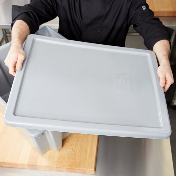 A person holding a grey plastic container lid.