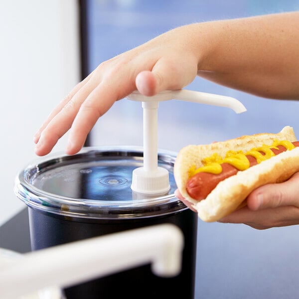 A person's hand using a Cambro cold crock to hold a hot dog with mustard and ketchup.
