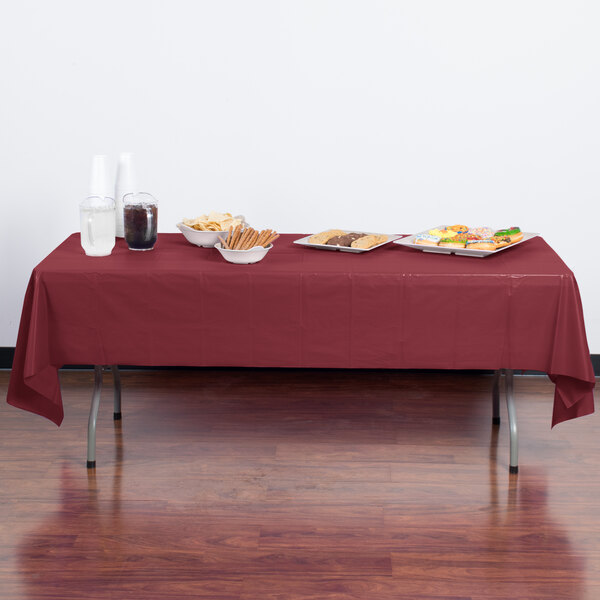 A burgundy rectangular plastic table cover on a table with food.