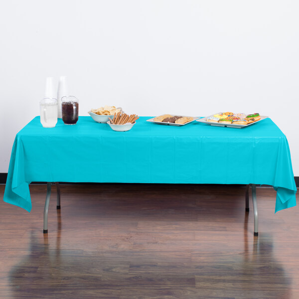 A table with Bermuda Blue Creative Converting plastic table cover and plates of food on it.