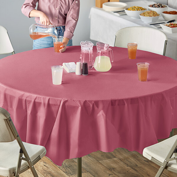 A woman pours white liquid into a glass on a table with a burgundy OctyRound tablecloth.