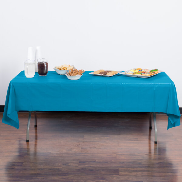 A table with turquoise blue Creative Converting plastic tablecloths on it with plates of food.