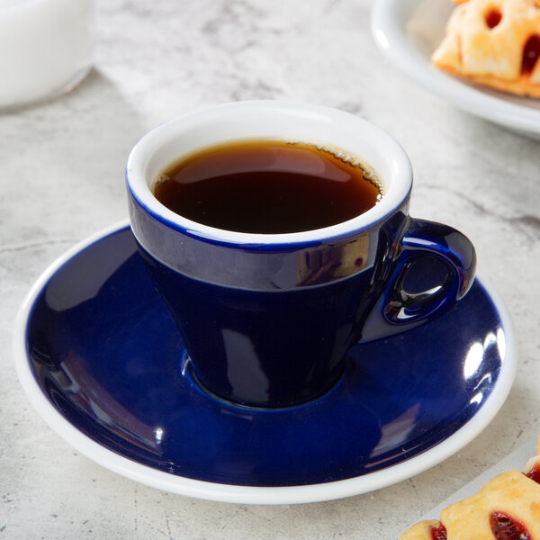 A blue CAC espresso cup and saucer with a plate of pastries on a table.