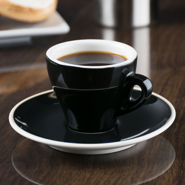 A black espresso cup on a saucer on a wooden table.
