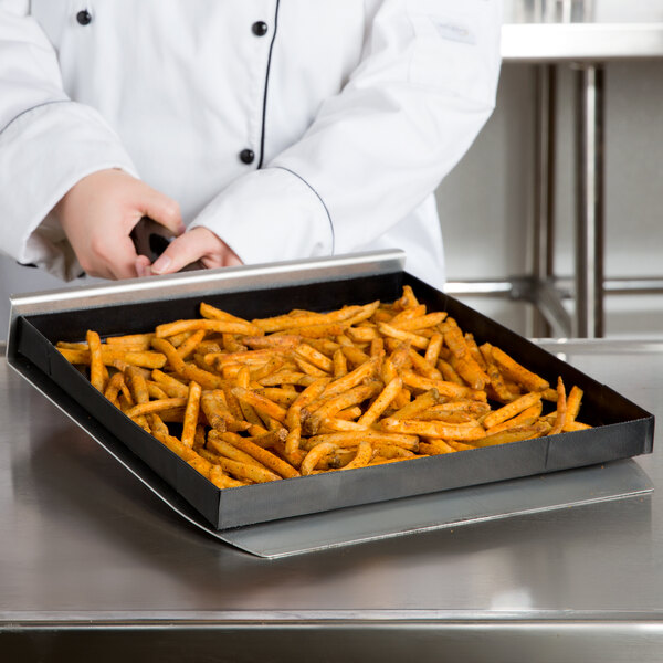 A chef using a TurboChef aluminum paddle peel to remove a tray of french fries from an oven.