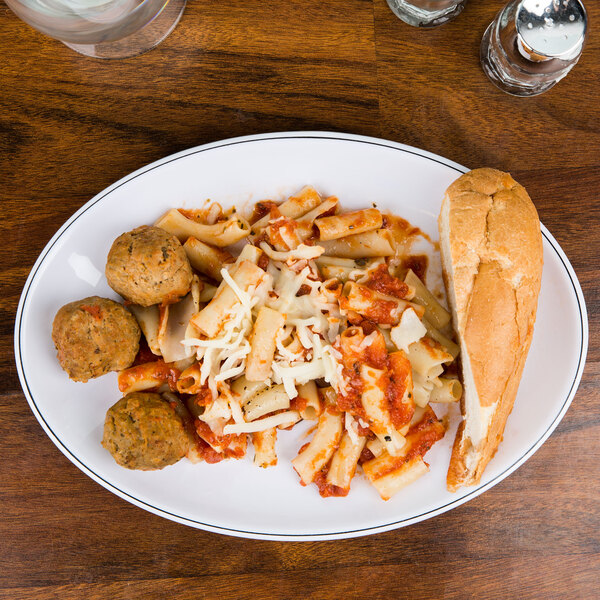 A white oval melamine plate with black trim holding pasta and meatballs.