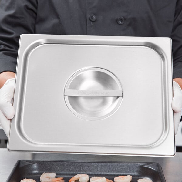 A chef using a Vollrath Super Pan V stainless steel cover on a metal tray of shrimp at a salad bar.