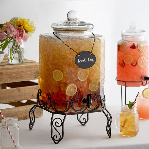 An Acopa glass beverage dispenser filled with fruity lemonade on a metal stand with a chalkboard sign.