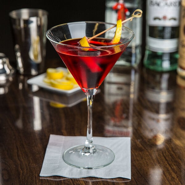An Arcoroc martini glass with red liquid and a lemon twist.