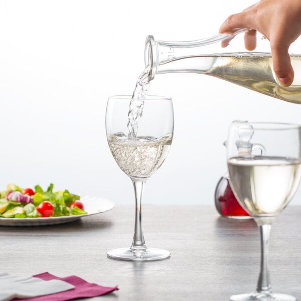 A hand pouring wine into an Arcoroc wine glass on a table.