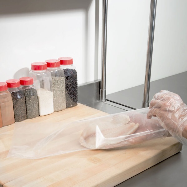 A person in gloves using an ARY VacMaster vacuum packaging bag to hold chicken.