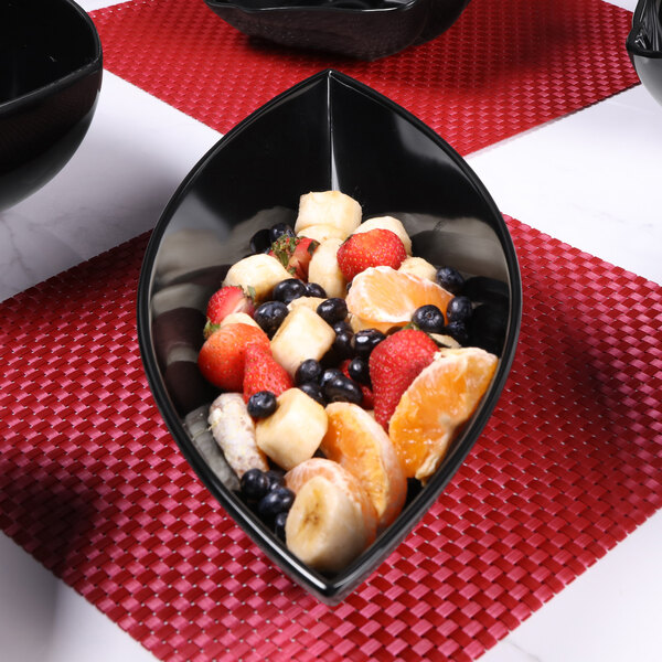 An Elite Global Solutions black melamine oval bowl filled with fruit on a table.