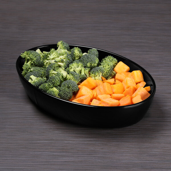 A black Elite Global Solutions oval bowl filled with broccoli and carrots on a table.