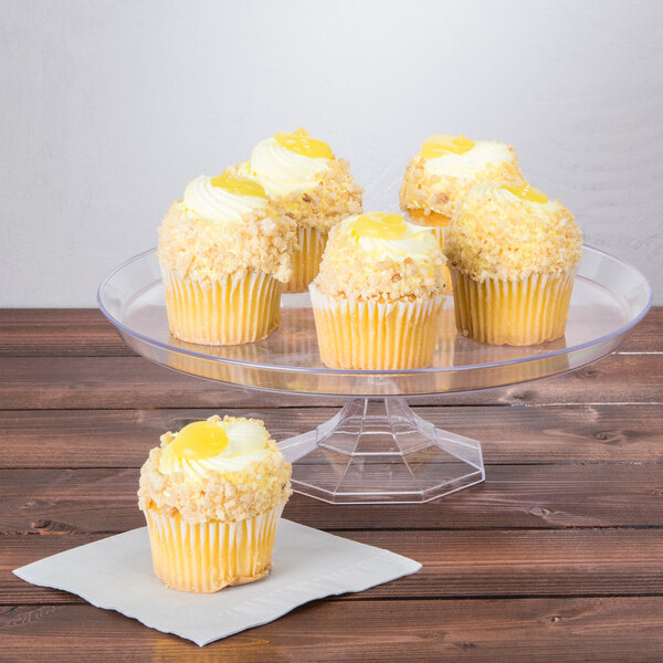 A Fineline clear plastic cake stand with a cupcake with yellow frosting and a yellow yolk on top on it.