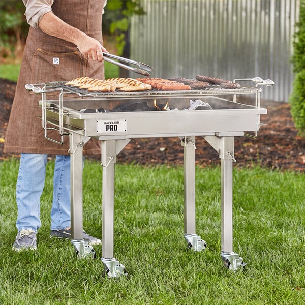 A man standing next to a Backyard Pro stainless steel charcoal grill cooking meat.