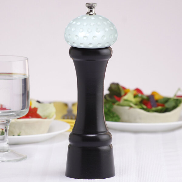 A black Chef Specialties pepper mill with a white golf ball on a table.