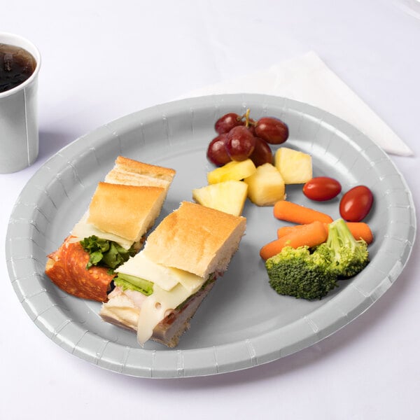 A Creative Converting shimmering silver oval paper platter with a sandwich, fruit, and vegetables on it.