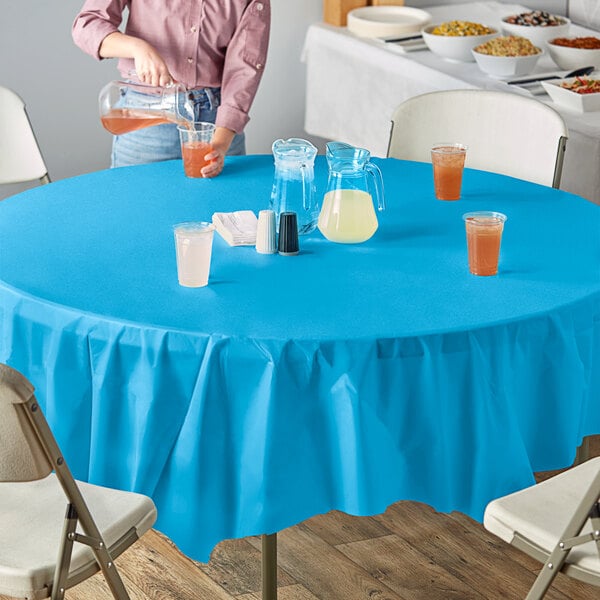 A woman sitting at an outdoor table with a turquoise blue tablecloth and glasses of liquid.