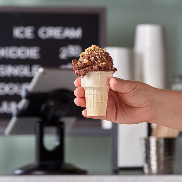 A hand holding a JOY gluten-free cake cone filled with chocolate ice cream.