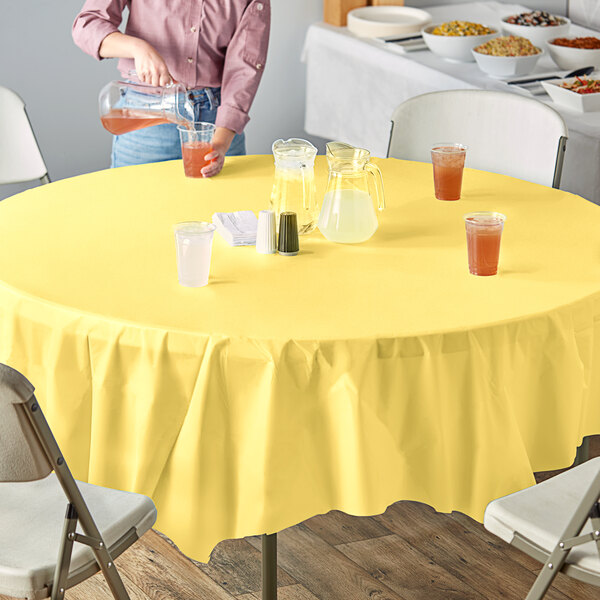 A table with a Mimosa Yellow Creative Converting round tablecloth with glasses of yellow and white liquid on it.