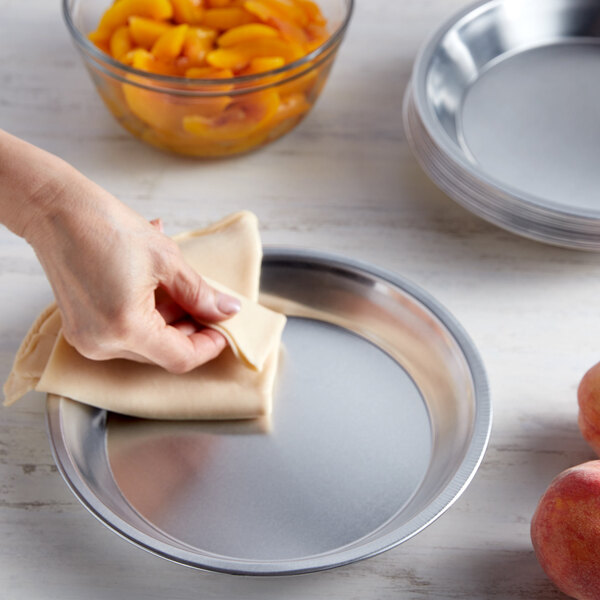 A hand wiping a Chicago Metallic aluminum pie pan with a cloth.