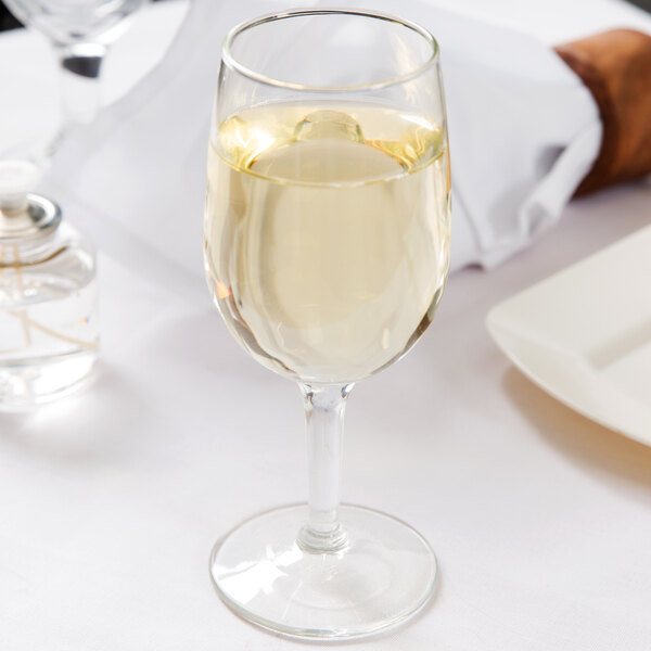 A Libbey tall wine glass filled with white wine on a table.