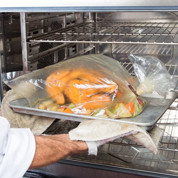 A person holding a tray of food in a Kenylon plastic cooking bag in an oven.