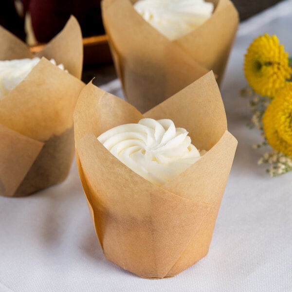 A Hoffmaster unbleached natural tulip baking cup with a cupcake decorated with white frosting and a yellow flower.